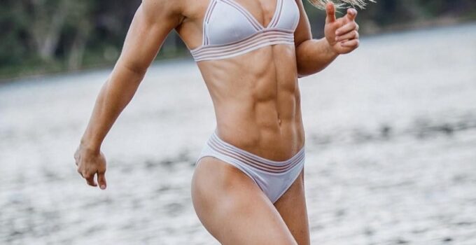 Claire P Thomas running by the lake in her bathing suit, smiling, looking ripped