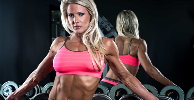 Whitney Jones leaning against dumbbells in the gym, looking fit and lean
