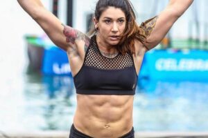 Kat Leone lifting heavy barbell overhead during a crossfit contest