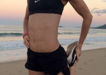 Cass Olholm stretching on the beach in her sports suit