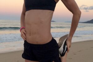 Cass Olholm stretching on the beach in her sports suit