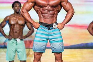 Diogo Montenegro posing on the Men's Physique stage, showcasing his ripped chest, arms, and midsection