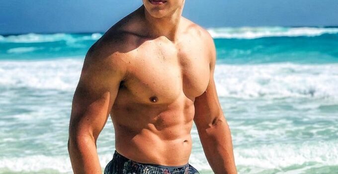 Gabriel Arones standing shirtless on the beach with black sunglasses, looking fit and strong