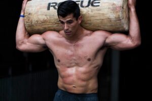 Garret Fisher shirtless, carrying heavy log over his head