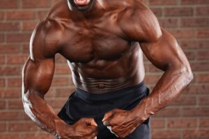 Gideon Akande flexing his muscles for a photo with a yelling grimace