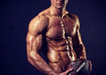 Josh Watson posing shirtless with a rugby ball, looking muscular and ripped
