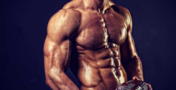 Josh Watson posing shirtless with a rugby ball, looking muscular and ripped