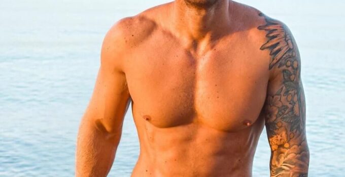 Matt Fox standing shirtless on the beach smiling for the photo, looking fit and lean