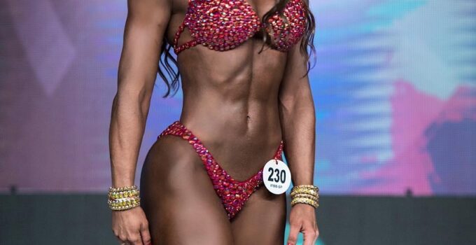 Pri Santtana standing on a bodybuilding stage smiling at the judges