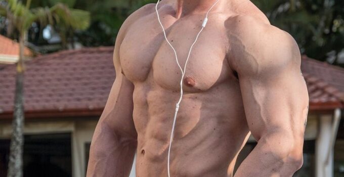 Rafael Rey standing shirtless outdoors with headphones on, looking swole and ripped