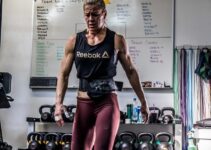 Rebecca Voigt Miller in a CrossFit gym with kettlebells behind her back, looking exhausted from training
