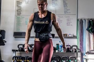 Rebecca Voigt Miller in a CrossFit gym with kettlebells behind her back, looking exhausted from training