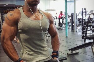 Antonio Mitchell showing his ripped physique in a grey tank top in the gym