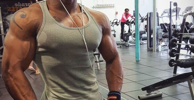 Antonio Mitchell showing his ripped physique in a grey tank top in the gym