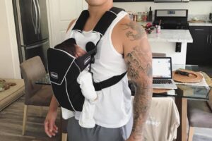 Bart Kwan carrying his child in a front facing baby carrier and smiling at the camera