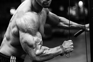 Julian Smith training shirtless with cables in a gym looking ripped