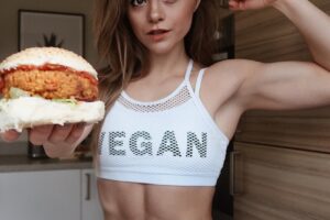 Stefanie Moir posing for a photo with a vegan burger in her hand looking fit and healthy